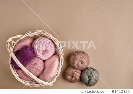 Balls of yarn and knitting needles. Colored yarn for knitting in a wicker bowl on a beige background. Balls of yarn and knitting needles. Colored yarn for knitting in a wicker bowl on a beige background. 91412533