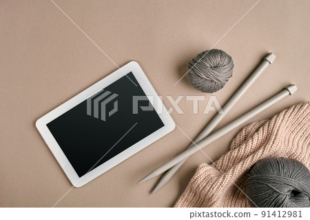 Gray knitting yarn ball, knitting needles and a tablet with a black screen, top view 91412981