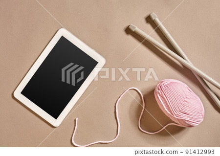 Pink knitting yarn ball, knitting needles and a tablet with a black screen, top view 91412993