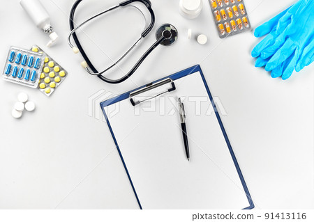 Medical equipment : pills, blue gloves, thermometer and stethoscope, white blank with a pen on white background. Top view. Copy space Medical equipment : pills, blue gloves, thermometer and stethoscope, white blank with a pen on white background. Top view. Copy space 91413116