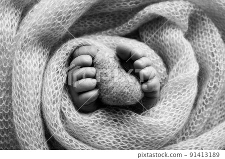 Knitted heart in the legs of a baby. Soft feet of a new born in a wool blanket. Close-up of toes, heels and feet of a newborn. Macro black and white photography the tiny foot of a newborn baby. Knitted heart in the legs of a baby. Soft feet of a new born in a wool blanket. Close-up of toes, heels and feet of a newborn. Macro black and white photography the tiny foot of a newborn baby. 91413189