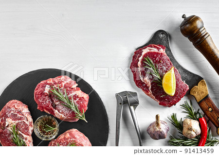 Fresh raw beef steaks with herbs, garlic, olive oil, pepper, salt and rosemary on black board: Tenderloin, Striploin, Rib Eye 91413459