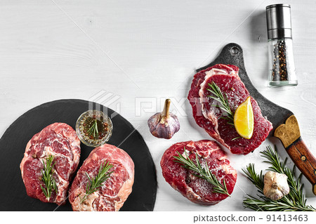 Fresh raw beef steaks with herbs, garlic, olive oil, pepper, salt and rosemary on black board: Tenderloin, Striploin, Rib Eye Fresh raw beef steaks with herbs, garlic, olive oil, pepper, salt and rosemary on black board: Tenderloin, Striploin, Rib Eye 91413463