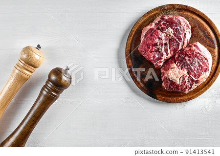 Raw beef steak with spices and ingredients for cooking on wooden cutting board and white background. 91413541