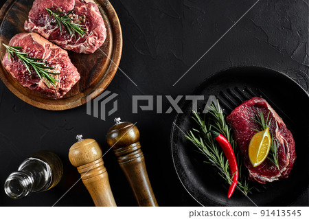 Fresh raw meat. Beef Tenderloin and marbled beef steaks on grill pan and frying board with seasoning, black background top view. 91413545