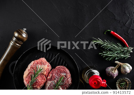 Fresh raw meat. Beef Tenderloin and two marbled beef steaks on grill pan and frying board with seasoning, black background top view. 91413572