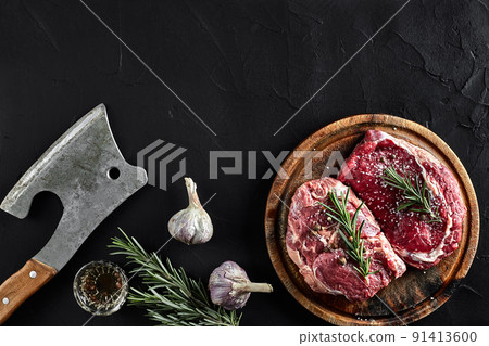 Piece of beef tenderloin, with ax for cutting and chopping meat, spices were cooking - rosemary, pepper, salt, garlic. On old wooden board on stone black table. Piece of beef tenderloin, with ax for cutting and chopping meat, spices were cooking - rosemary, pepper, salt, garlic. On old wooden board on stone black table. 91413600