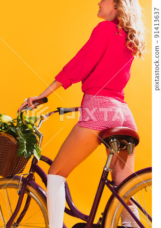 Portrait of beautiful young girl in pink outfit posing with retro bike isolated over yellow studio background. Colorful image 91413637