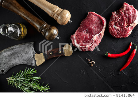 Piece of beef tenderloin, with ax for cutting and chopping meat, spices were cooking - rosemary, pepper on old black table. Top view copy space Piece of beef tenderloin, with ax for cutting and chopping meat, spices were cooking - rosemary, pepper on old black table. Top view copy space 91413864