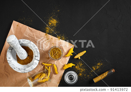 Turmeric Haldi powder in small bowl with raw whole in marble mortar over black background with copy space 91413972