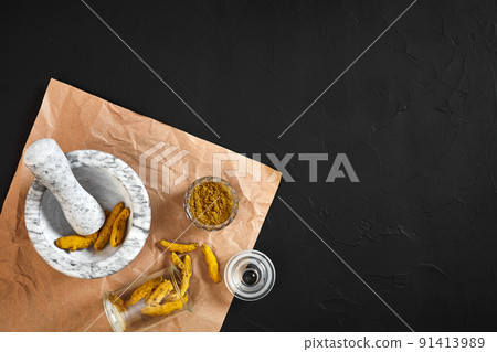 Turmeric Haldi powder in small bowl with raw whole in marble mortar over black background with copy space Turmeric Haldi powder in small bowl with raw whole in marble mortar over black background with copy space 91413989
