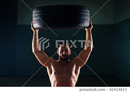 Muscular fitness man antique statue perfect muscles six pack abs and bare nude chest bodybuilder flipping tire wheel on a black background in the studio. Concept functional training workout gym Muscular fitness man antique statue perfect muscles six pack abs and bare nude chest bodybuilder flipping tire wheel on a black background in the studio. Concept functional training workout gym 91414613