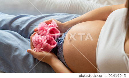 Pregnancy baby shoes. Happy pregnant woman holding pink baby shoes. Small child shoe. Concept of pregnancy, maternity, expectation for baby birth. 91414945
