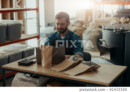 Business owner of small coffee roasting factory working laptop on his workplace Business owner of small coffee roasting factory working laptop on his workplace 91415589