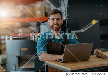 Warehouse worker of small coffee roasting factory working laptop on his workplace Warehouse worker of small coffee roasting factory working laptop on his workplace 91415591