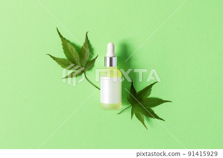 Glass bottle with medical CBD oil and fresh hemp leaves on green background top view. 91415929