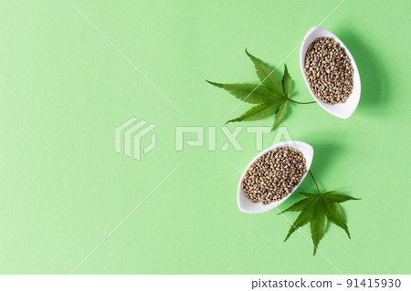 Medical cannabis seeds and fresh hemp leaves on green background top view. Medical cannabis seeds and fresh hemp leaves on green background top view. 91415930