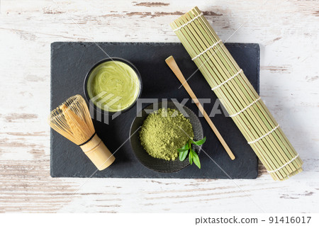 Green matcha tea drink and tea accessories on black board on white wooden table top view. Japanese tea ceremony concept. Green matcha tea drink and tea accessories on black board on white wooden table top view. Japanese tea ceremony concept. 91416017