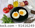 Fried eggs with vegetables, spices and herbs on light wooden background. Traditional European or Asian breakfast. 91416249