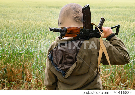A soldier with a machine gun stands in a field, Ukrainian wheat fields and war. A soldier with a machine gun stands in a field, Ukrainian wheat fields and war. 91416823
