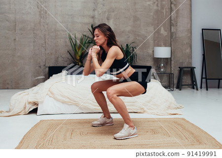 Young woman practicing squats. Woman exercising at home. 91419991
