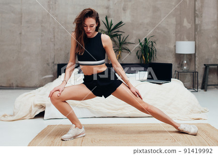 Woman practicing at home doing leg stretching exercises 91419992
