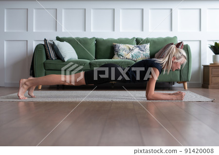 Young woman working out at home, doing plank exercise Young woman working out at home, doing plank exercise 91420008