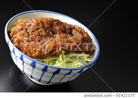 A sauce and a bowl with a cutlet entwined with plenty of sauce on top of shredded cabbage shot on a black background 91422177