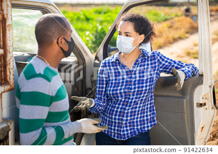 Man and woman farmers in protective masks signing papers and communicating near car on the field 91422634
