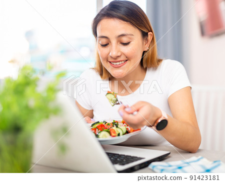 Housewife watching movie on laptop and eating vegetable salad Housewife watching movie on laptop and eating vegetable salad 91423181