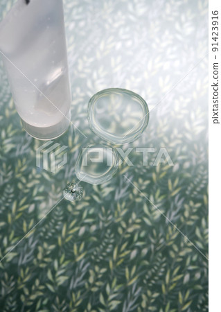 A transparent bottle of cosmetic gel on a green background with drops of the product. A transparent bottle of cosmetic gel on a green background with drops of the product. 91423916