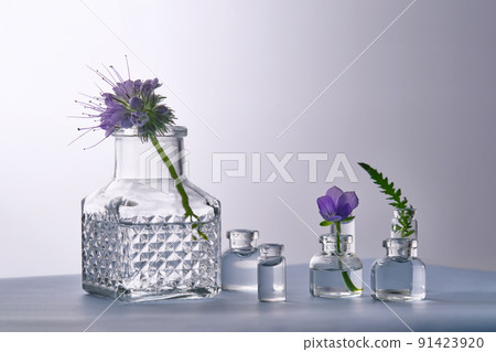 Different bottles of water with flowers on a light background. It can fit the theme of cosmetics, glass and freshness. 91423920