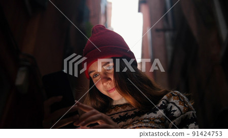 Woman in a dark alley between buildings. Looks into her phone. Woman in a dark alley between buildings. Looks into her phone. 91424753