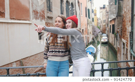 Two young women walk the streets of Venice - One of them show something to other Two young women walk the streets of Venice - One of them show something to other 91424770