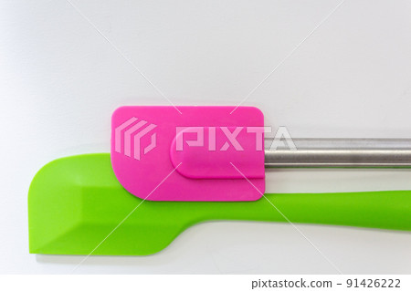 Two silicone spatulas, one is green and the another is pink lay on white background 91426222
