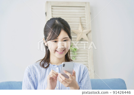 A woman who uses a smartphone with a smile in the living room 91426446