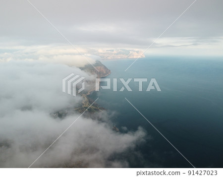 Aerial view. Blue sky sun and fog over calm sea. The drone flies over foggy and fluffy clouds. Abstract aerial nature summer ocean sunset sea and sky background. Vacation, travel and holiday concept. 91427023