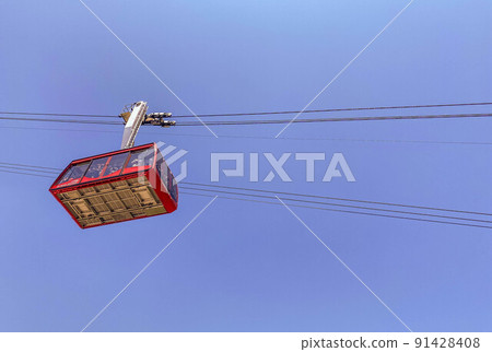 cable car on the mountain. cabin with tourists moves on black, thick cables at a great height. red cabin with large windows for visibility cable car on the mountain. cabin with tourists moves on black, thick cables at a great height. red cabin with large windows for visibility 91428408