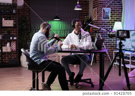 Multiethnic team of people broadcasting internet podcast, recording video discussion on camera. Influencer and guest talking on online livestream to create social media channel content. Multiethnic team of people broadcasting internet podcast, recording video discussion on camera. Influencer and guest talking on online livestream to create social media channel content. 91428705