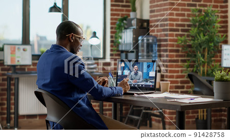 Businessman talking to manager on online teleconference call in startup office, meeting with leader on remote videocall telecommunication. Chatting on videoconference with headphones. Businessman talking to manager on online teleconference call in startup office, meeting with leader on remote videocall telecommunication. Chatting on videoconference with headphones. 91428758