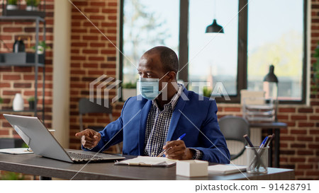 Businessman taking notes on company paperwork during covid 19 pandemic, working with website statistics on documents. Young employee planning strategy on online network. Tripod shot. Businessman taking notes on company paperwork during covid 19 pandemic, working with website statistics on documents. Young employee planning strategy on online network. Tripod shot. 91428791