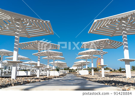 Rows of wooden umbrellas from the sun on the seashore in the morning. Wooden paths on the sand between umbrellas. Beach holiday at the resort. 91428884