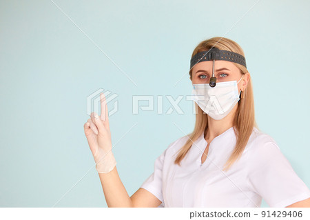 Female ENT doctor, wearing in mask at the studio looking at the camera and points her finger at the wall 91429406