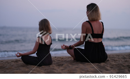 Mom and daughter do yoga and meditate on beach 91429665