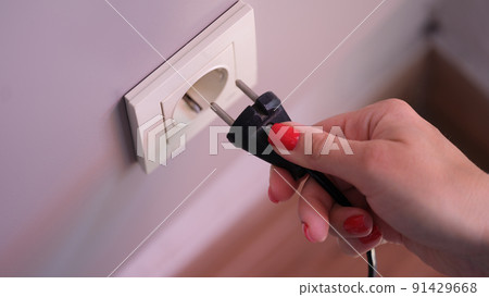 Connecting black electric plug with hand to white plastic socket on awhite wall 91429668