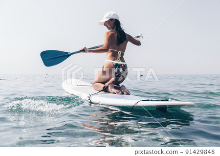 SUP Stand up paddle board. Young woman sailing on beautiful calm sea with crystal clear water. The concept of an summer holidays vacation travel, relax, active and healthy life in harmony with nature. 91429848