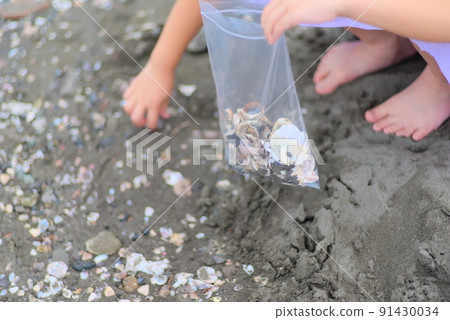 A scene where a child is picking up shells on a sandy beach 91430034