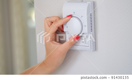 Woman's hand regulating the temperature of central heating of house on thermostat Woman's hand regulating the temperature of central heating of house on thermostat 91430135
