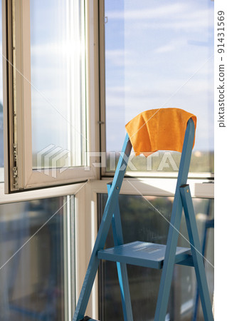 Orange rag on a blue ladder near panoramic window in apartment. 91431569