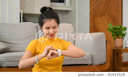 Pretty young woman setting, checking her heart rate data on smartwatch during morning workout at home 91433320